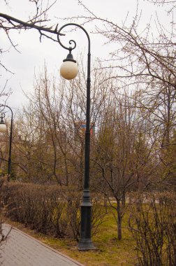 Bulutlu bir bahar gününde parkta sokak ve fener.