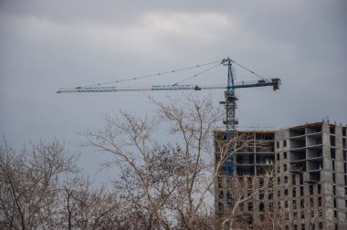İnşaat alanı. Büyük endüstriyel vinç, bitmemiş yüksek binalar ve arka planda mavi gökyüzü. Darağacı. Modern inşaat mühendisliği. Çağdaş şehir manzarası.