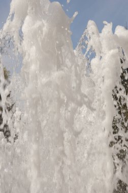 Bir sürü kabarcık ve su sıçraması olan şekilsiz bir köpük akıntısı, bulutlarla mavi gökyüzüne doğru fışkırıyor. Kapat..