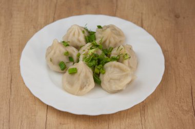 Beyaz bir tabakta yeşil soğan serpiştirilmiş khinkali.