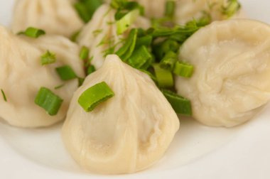 Beyaz bir tabakta yeşil soğan serpiştirilmiş khinkali.