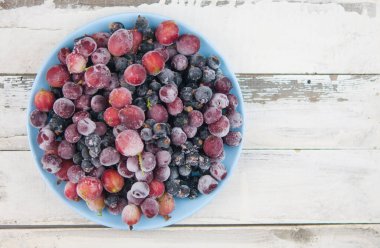 Donmuş meyve arkaplanı seramik tabakta. Meyveler buzlu. antika beyaz tahta tahtalar üzerinde, metin için boşluk, kopyalama alanı