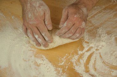 Pişirme konsepti. Tanınmayan bir adamın elleri ahşap masa arkasında hamur yoğurur. Erkek fırıncı.