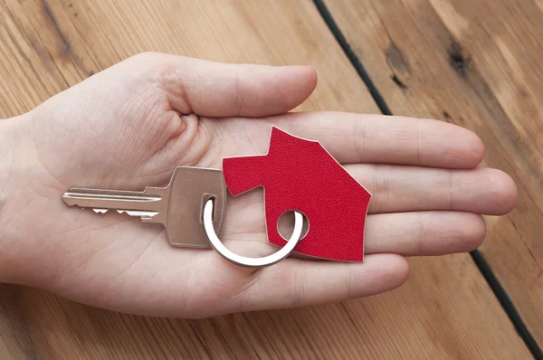 Human hand holding house key on a wood background — Stock Photo, Image