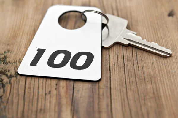 Ahşap masa üzerindeki 100 Oda numarasıyla otel Süiti anahtarı — Stok fotoğraf
