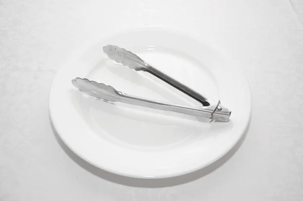 Steel tongs on white dish — Stock Photo, Image