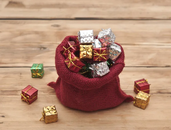 Färgglada presentförpackning med band och rosetter och röd säck på woode — Stockfoto