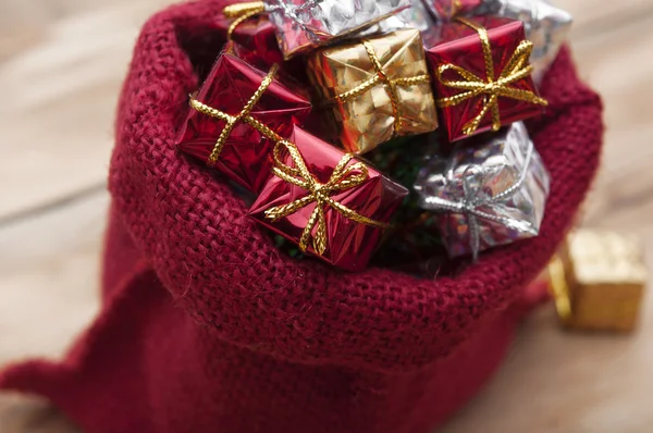 Färgglada presentförpackning med band och rosetter och röd säck på woode — Stockfoto