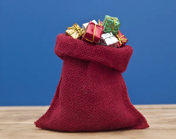Scatole regalo colorate con nastri e fiocchi e sacco rosso su legno — Foto Stock