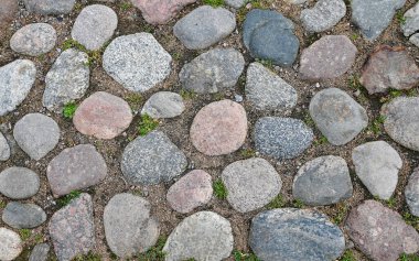 Düzensiz şekilli taşlar, doğal dokular ve toprak tonlarını gösteren kaldırıma yakın çekim. Eski yüzey, geleneksel taş yolların güzelliğini vurgular..