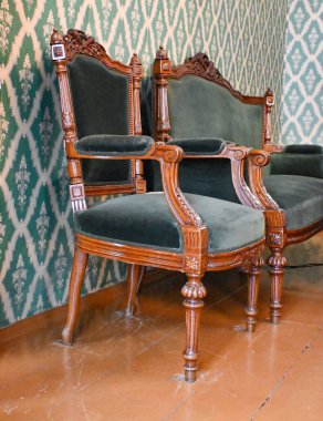 Gri bir duvar ve zemine karşı iki klasik koltuk. Boşluğu kopyala