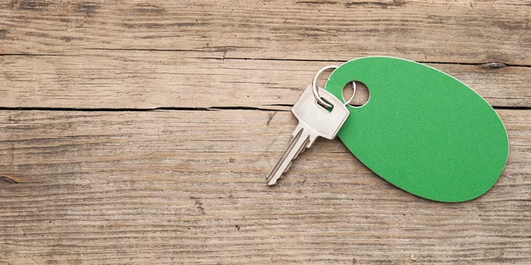 Key with a blank label on an old wooden plank — Stock Photo, Image