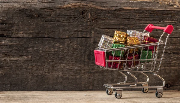 Einkaufswagen mit Geschenkboxen über Holzhintergrund — Stockfoto