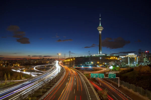 Carreteras de Teherán llenas de coches de paso frente a la Torre Milad contra el cielo azul con nubes — Foto de Stock