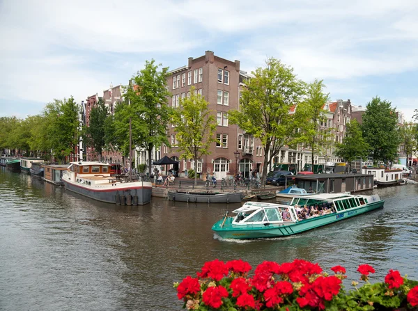 Лодка с людьми на борту плывет по каналу в Амстердаме со старыми зданиями — стоковое фото