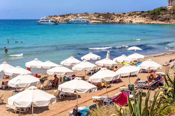 PAPHOS, CHYPRE - 24 JUILLET 2016 : Touristes, chaises longues et parasols lors d'une chaude journée d'été à la plage de Coral Bay . — Photo