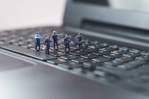 Миниатюрный полицейский отряд защищает ноутбук. Технологическая концепция — стоковое фото