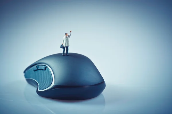Мініатюрний бізнесмен махає на вершині комп'ютерної миші. Бізнес — стокове фото
