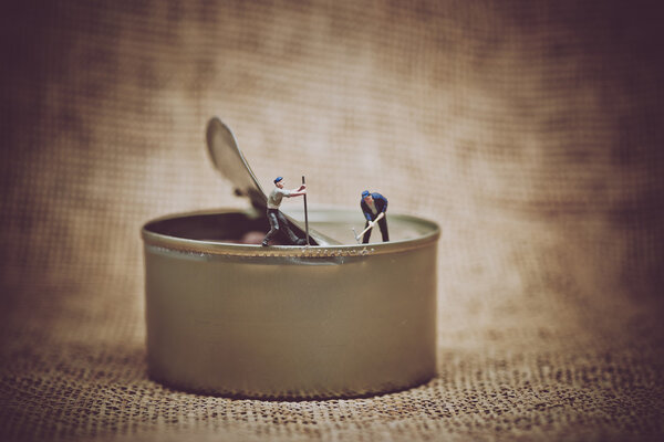 Miniature workers opening a can. Color tone tuned photo.
