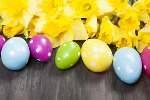 Ovos de Páscoa coloridos e narcisos de primavera no fundo de papel — Fotografia de Stock