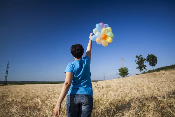 Mujer joven con globos de colores en el campo de verano — Foto de Stock