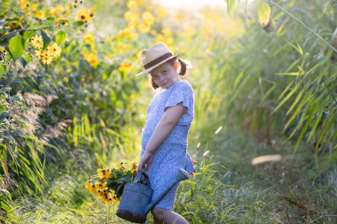 Küçük bir yolda yürüyen küçük bir kız elinde kaliteli bir sulama kabıyla sonbahar çiçekleriyle dolu..