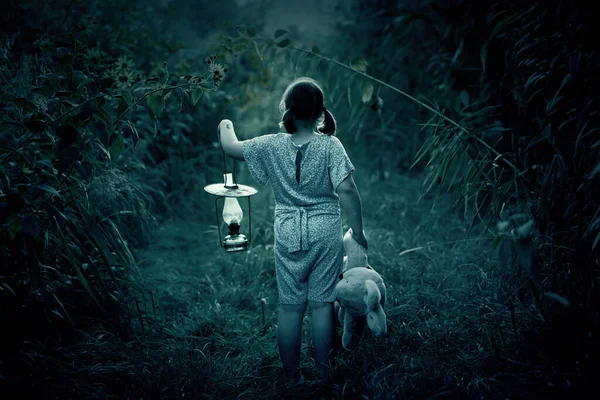 小さな女の子がテディとランタンを持って暗い森の中を歩いている ハロウィンのコンセプト — ストック写真