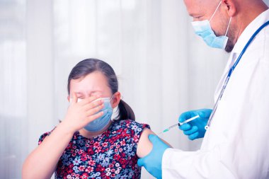 Çocuklar aşılama konsepti. Doktor, korkmuş küçük bir kızın koluna yüz maskesi aşısı yapıyor..