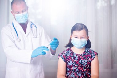 Çocuklar aşılama konsepti. Doktor yüz maskesi takan küçük bir kızın koluna aşı yapıyor..