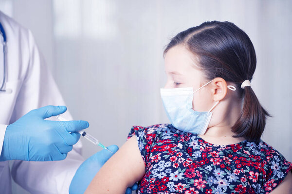 Дети прививают концепцию иммунизации. Врач вводит вакцину в руку маленькой девочки в маске для лица
.