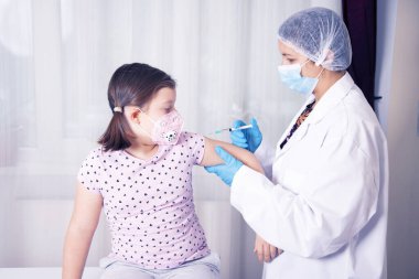 Çocuklar aşılama konsepti. Doktor yüz maskesi takan küçük bir kızın koluna aşı yapıyor..