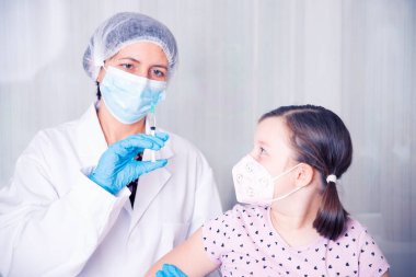 Çocuklar aşılama konsepti. Doktor yüz maskesi takan küçük bir kızın koluna aşı yapıyor..
