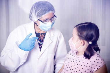 Çocuklar aşılama konsepti. Doktor yüz maskesi takan küçük bir kızın koluna aşı yapıyor..