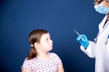 Çocuklar aşılama konsepti. Doktor yüz maskesi takan küçük bir kızın koluna aşı yapıyor..