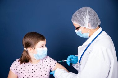 Çocuklar aşılama konsepti. Doktor yüz maskesi takan küçük bir kızın koluna aşı yapıyor..