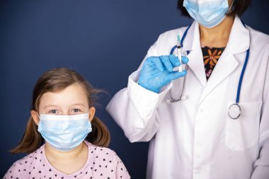 Çocuklar aşılama konsepti. Doktor yüz maskesi takan küçük bir kızın koluna aşı yapıyor..