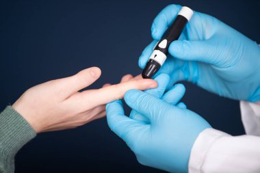 Kan şekeri seviyesini ölçmek için parmak üzerinde mızrak kullanarak doktor ellerini kapat. 