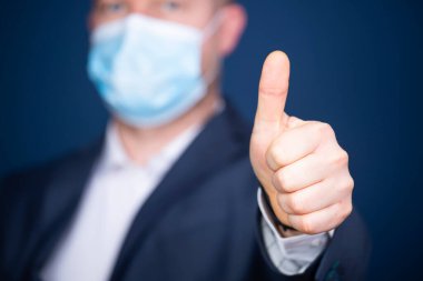 Tıbbi maskeli bir iş adamı onay işareti ya da baş parmağını kaldırdı. İş ya da hizmet konseptinin mükemmelliği.