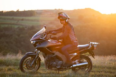 Gün batımında arka planda genç motosiklet sürücüsü.