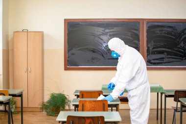 İşçi COVID-19, Coronavirüs 'ün okullara yayılmasına karşı önleyici önlemlerin bir parçası olarak dezenfektan püskürtür. Yeni okul sezonuna hazırlanıyorum..
