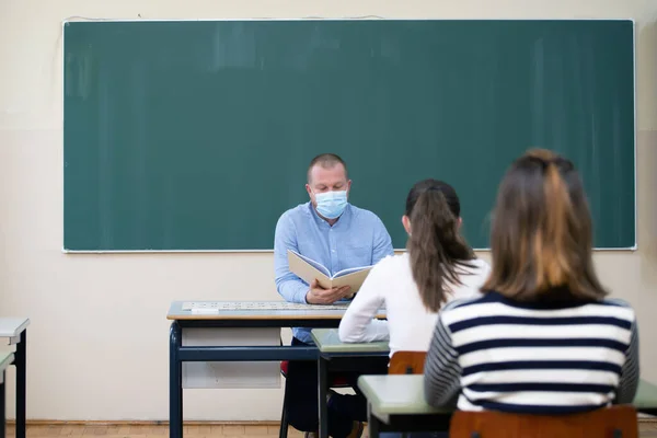 Students in protective face masks studying in classroom with teacher. Precautions in coronavirus pandemic