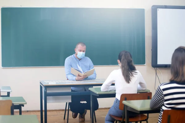 Students in protective face masks studying in classroom with teacher. Precautions in coronavirus pandemic