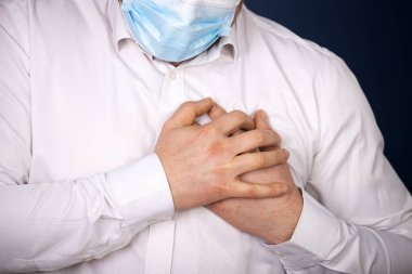 Göğüs ağrısı olan tıbbi yüz maskesi takan bir adam. Kalp krizi, iş yerinde nefes darlığı..