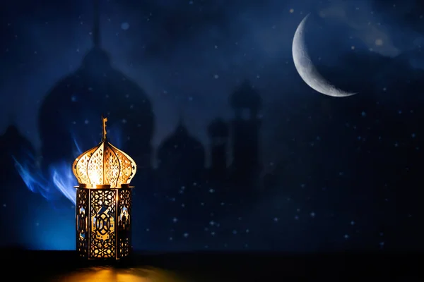 Ornamental Arabic lantern with crescent moon glowing at night. Festive greeting card for Muslim holy month Ramadan Kareem.