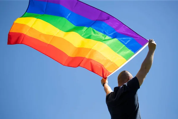 男人拿着同性恋彩虹旗在蓝色的夏日天空 双性恋 同性恋 女同性恋 变性人的象征 同性夫妇的幸福 自由和爱的概念 — 图库照片