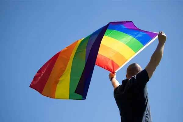 青い夏の空にゲイ レインボー フラッグを掲げる男 バイセクシャル レズビアン トランスセクシャルのシンボル 同じセックスカップルのための幸福 自由と愛の概念 — ストック写真
