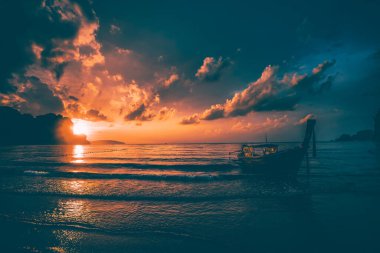 Tayland, Krabi 'deki Railay Plajı' nda dramatik bir gün batımı, ön planda geleneksel uzun kuyruklu tekne..