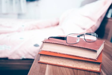  Güneşli bir sabahta yatak odasındaki komodinin üstünde kitap ve gözlük.