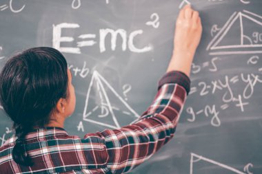 Öğretmen ya da öğrenci ders sırasında tahtaya yazı yazıyor ve sınıfta ders veriyor..