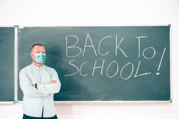 Teacher with face mask welcoming children back at school after lockdown. Back to school during COVID-19 pandemic.